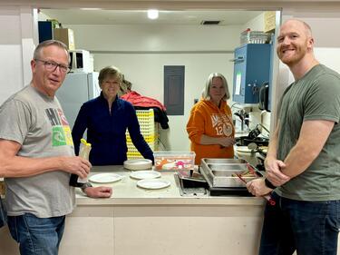 4 Adults standing at a counter who support the community breakfast program at the school